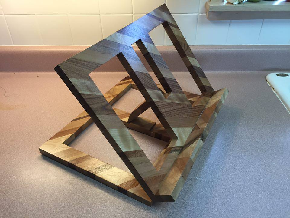 From Jerry Van Dyke: Here's a cookbook holder I made for my oldest daughter. 37 pieces of cherry, mesquite, and birch glued together to make two solid pieces and then the insides cut out. Those two pieces are hinged together and the support arm is attached via a hinge. Finished with a semi-gloss clear coat.