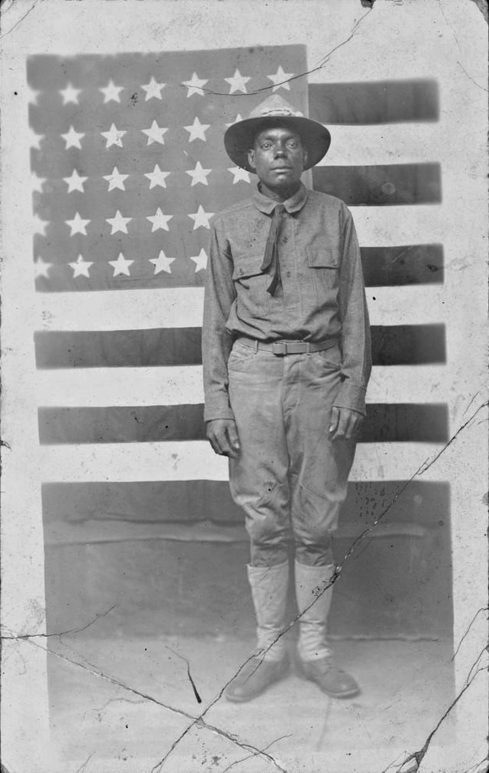WWI soldier in uniform standing in front of American flag.
