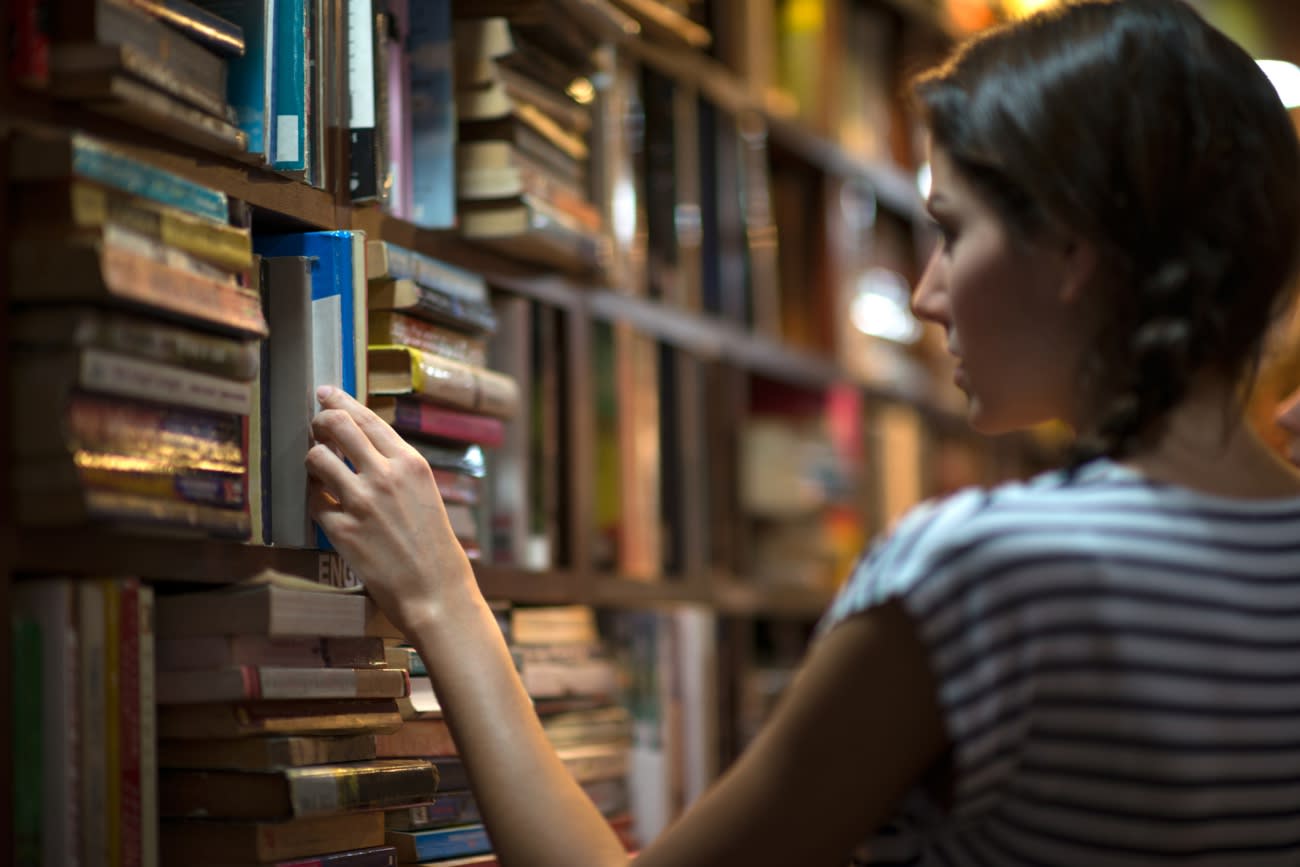 Beautiful woman looking at books in a library. Ambient light to emphasize the mood and location. Converted from RAW.