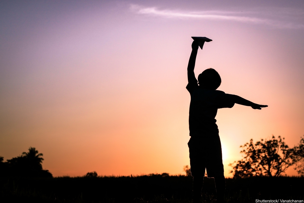 little boy playing with a paper airplane at sunset