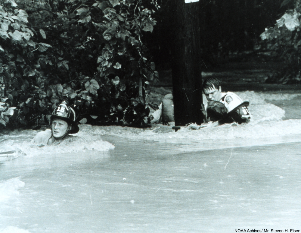Dragging a rescued individual back to safety through the strong current The rescued man was lucky - many people have been killed by flash floods. Rockville, Maryland. July 15, 1975