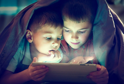 Two brothers share a tablet in the dark under a blanket