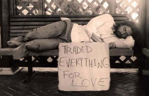 A man sleeps on a bench with a sign of his sacrifice.