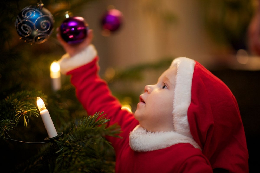 child in Santa suit decorating Christmas tree