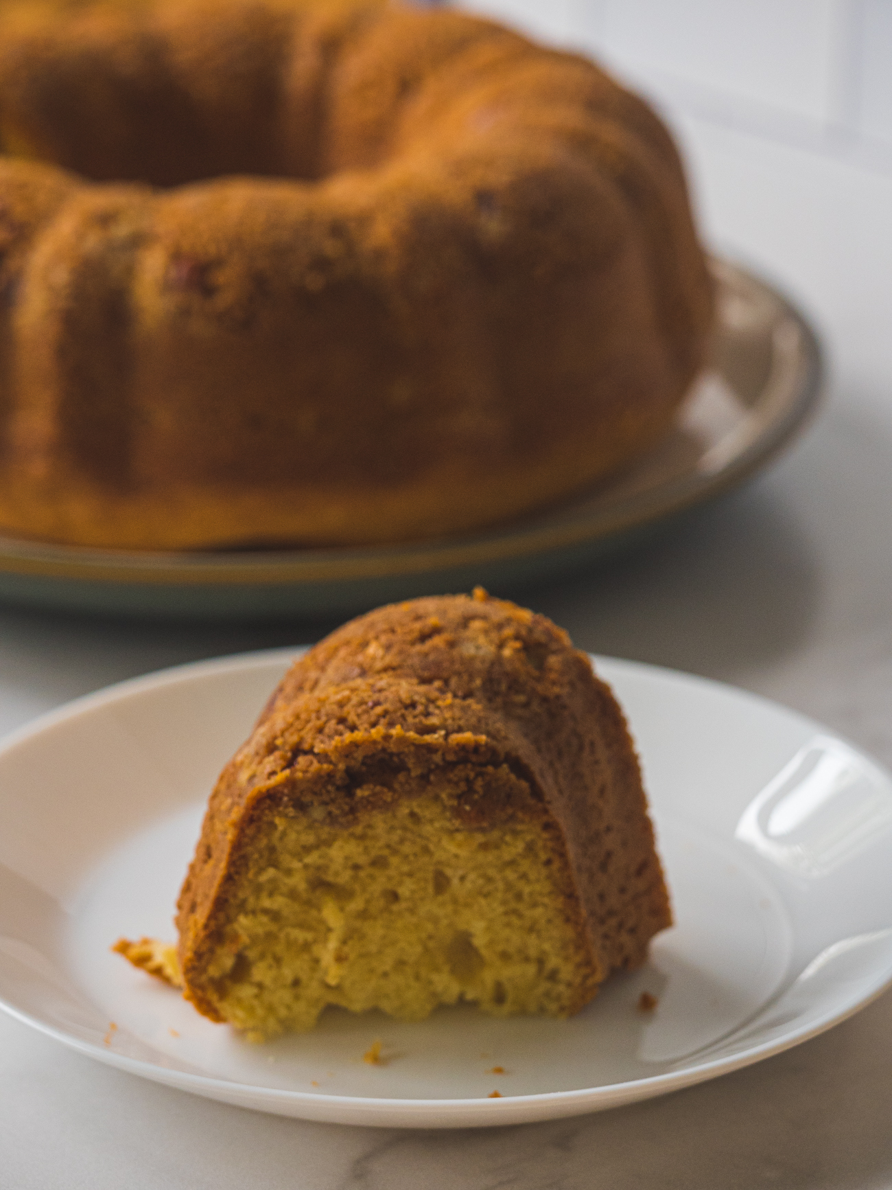 slice of sour cream coffee cake with rest of cake in background