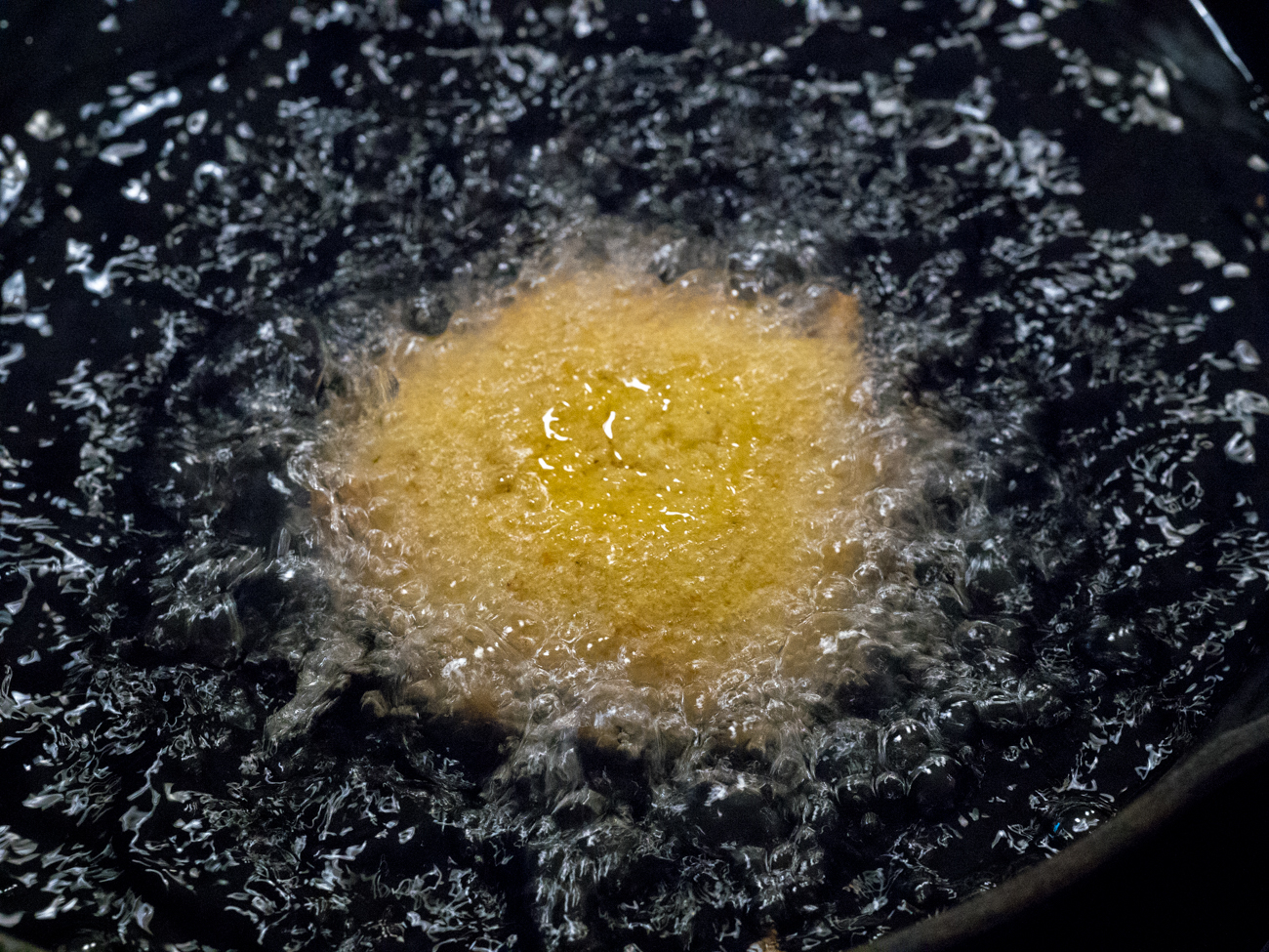 hot water cornbread being fried in oil in cast iron skiller