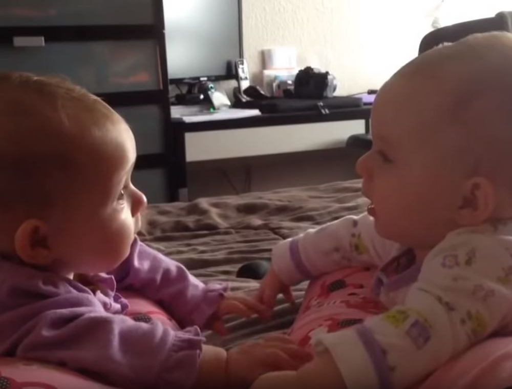 twin babies talking and holding hands