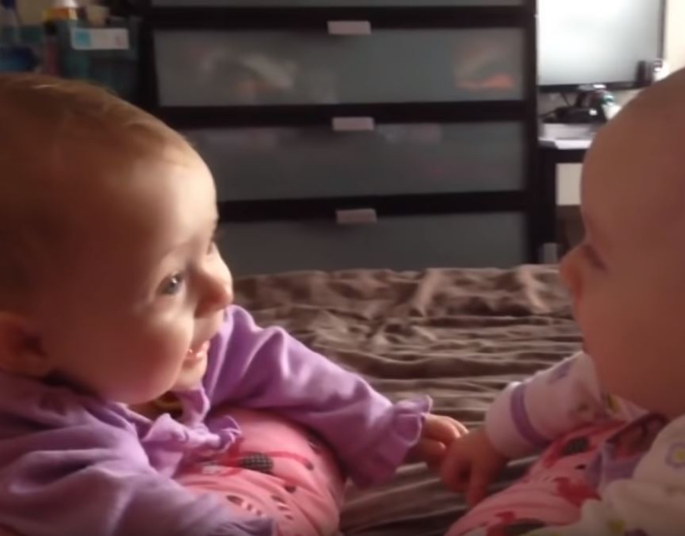 twin babies talking and holding hands