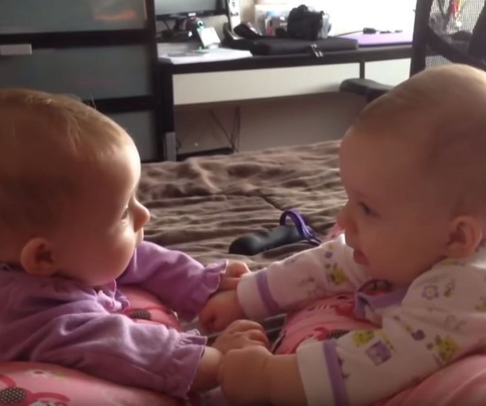 twin babies talking and holding hands