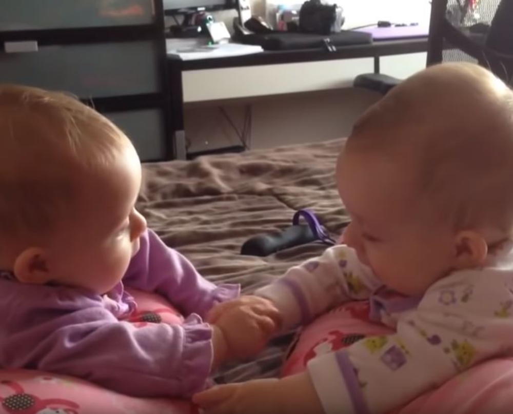 twin babies talking and holding hands